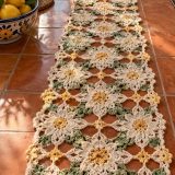 Cream and yellow daisy motif crochet table runner with sage green leaf clusters laid down a wooden table in sunlight