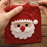 Red granny square with layered Santa face applique, white scalloped beard, red hat and pompom on wooden table